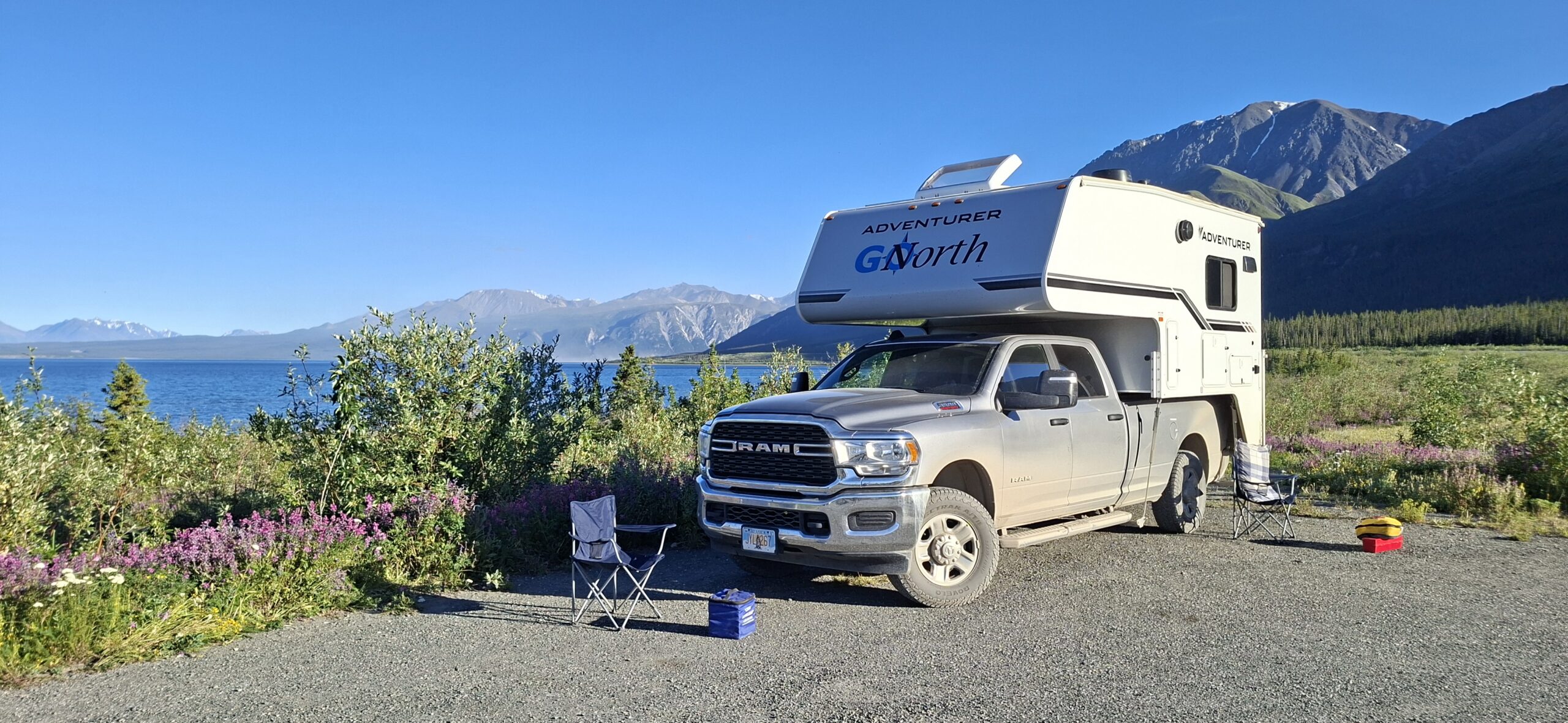 Een truck camper geparkeerd naast een meer omringd door bergen in Yukon