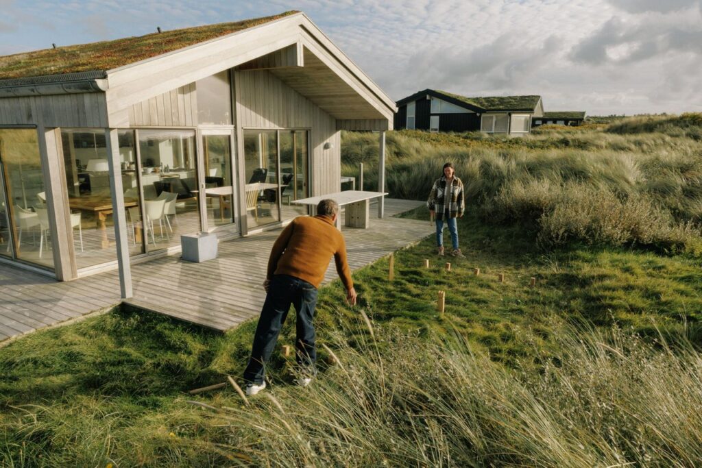 Vakantiehuis in de Deense duinen met ruim terras en twee reizigers die buiten een spel spelen